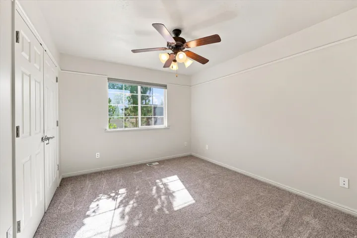 Neutral-toned wall paint, textured carpeting, contemporary ceiling fan with lighting, white trim work, and a window with natural light