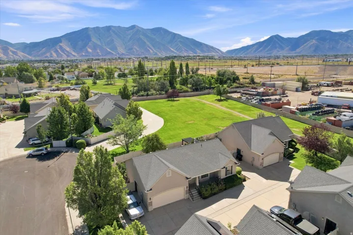 Property featuring a light-colored exterior, an attached garage, a paved driveway, and a shingled roof, all set against a distant mountain range