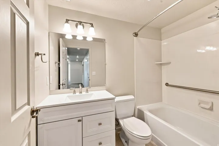 White vanity with integrated sink, three-light vanity fixture, large wall-mounted mirror, and a full-size bathtub with shower combination