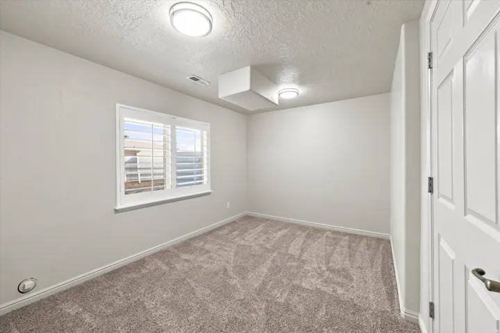 Neutral tone walls, textured ceiling, two flush-mount ceiling lights, louvered window shutters, and plush carpet flooring