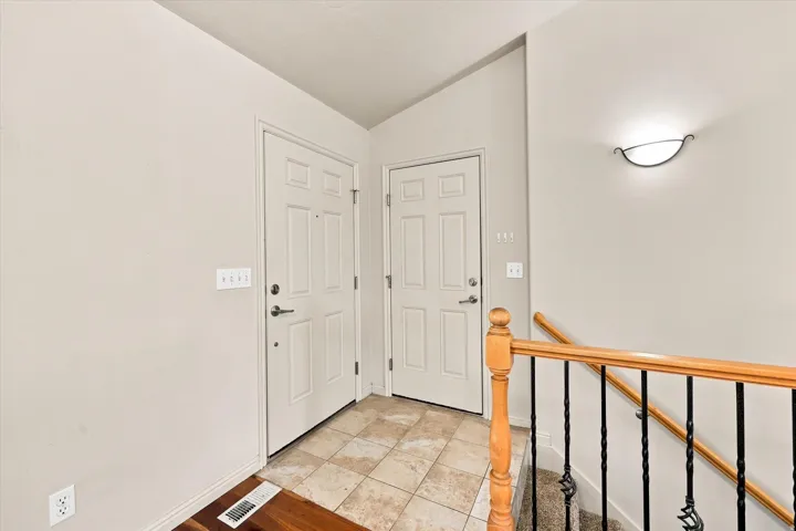 Tiled entryway with two paneled doors, hardwood-finish flooring, and a decorative wall sconce