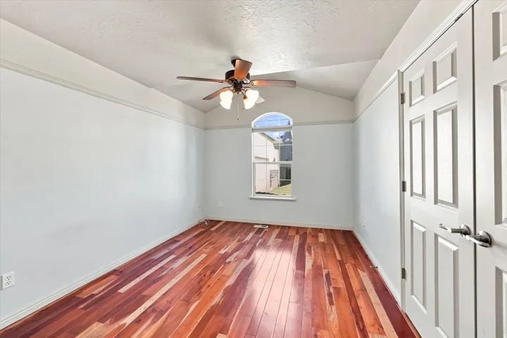 Vaulted ceiling with a ceiling fan, arched window, wood-finish flooring, and panel doors