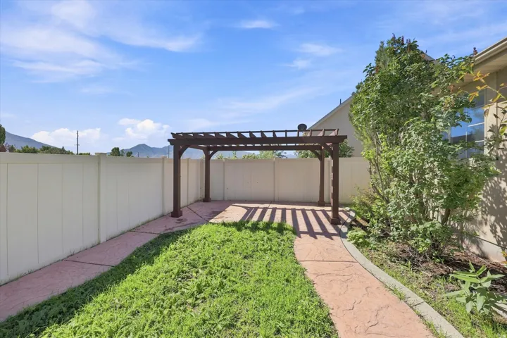 Backyard featuring a wooden pergola, concrete pathway, and perimeter fencing