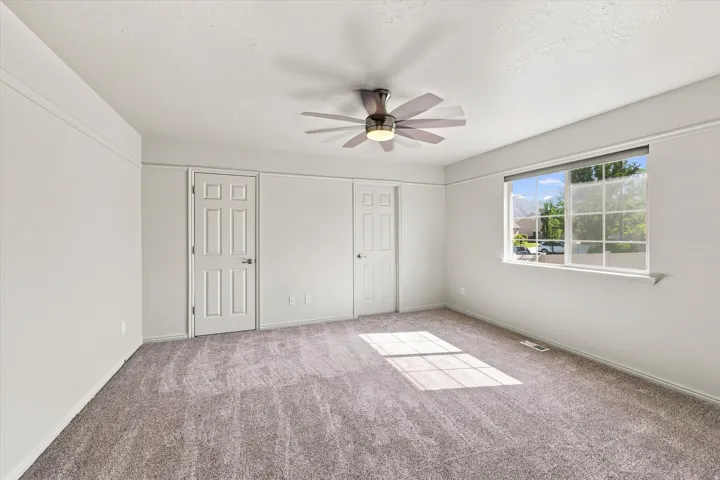 Carpeted room featuring a ceiling fan with integrated lighting, a large window, and two paneled doors