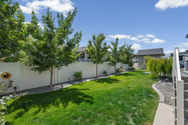 Expansive green lawn with mature trees, a white privacy fence, and a stone-lined garden bed