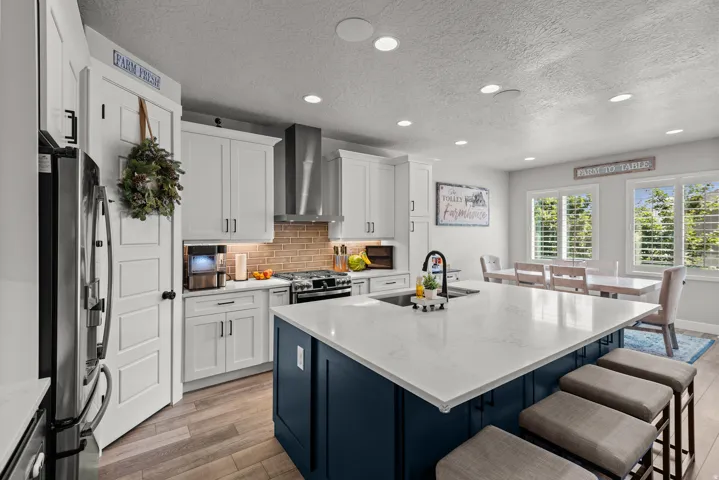 Modern kitchen featuring a large central island with a quartz countertop and integrated sink, white shaker cabinetry, stainless steel appliances, and wood-finish flooring