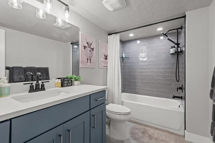 Modern bathroom featuring a single vanity with a white countertop and blue cabinetry, matte black fixtures, a built-in tub and shower combination with subway tile surround, and recessed lighting