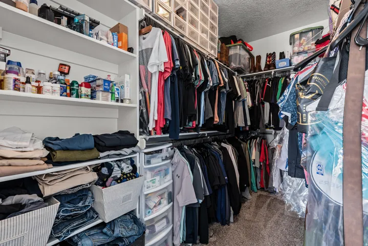 Spacious walk-in closet featuring extensive built-in shelving, double hanging rods with multiple tiers for organized storage, clear plastic storage bins, and carpet flooring