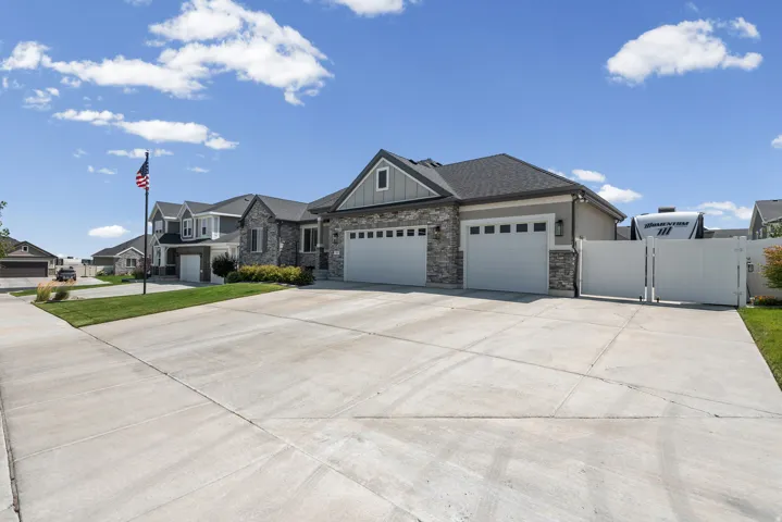 Contemporary exterior featuring a stone and siding facade, an attached three-car garage, and a wide concrete driveway