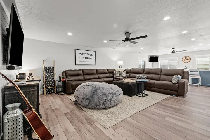 Spacious entertainment area featuring wood-finish flooring, recessed lighting, and white horizontal blinds