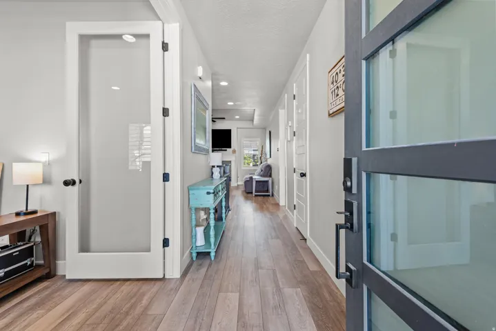 Expansive entry hallway with wood-finish flooring, recessed lighting, and a modern glass-paneled door with dark hardware