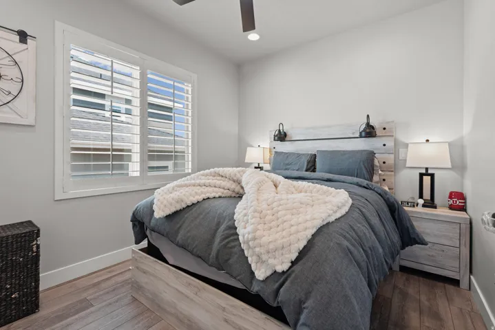 Room featuring wood-finish flooring, a window with louvered shutters, a ceiling fan, and light gray walls with white baseboards