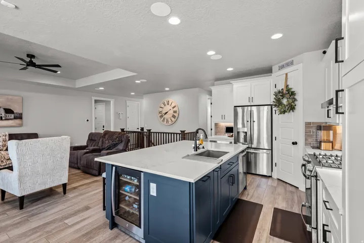 Kitchen featuring a large island with an integrated beverage cooler, white cabinetry, stainless steel appliances, and wood-finish flooring