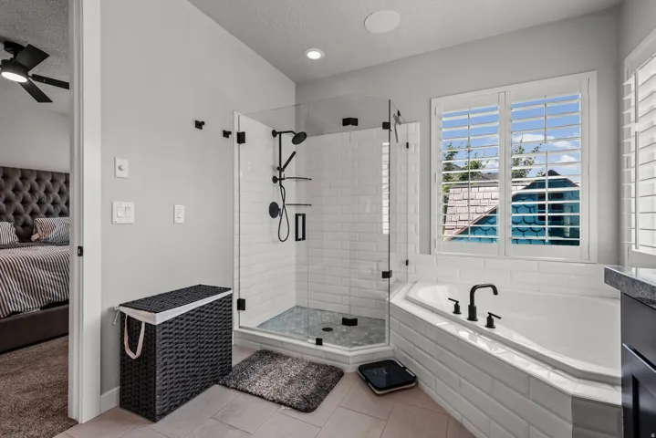 Modern bathroom featuring a glass-enclosed shower with subway tile surround, a built-in soaking tub with matte black fixtures, and a window with plantation shutters