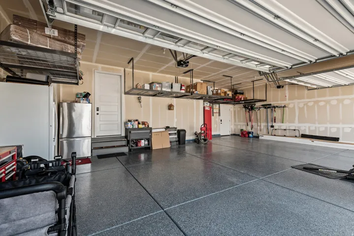 Spacious garage featuring a finished epoxy floor, overhead storage racks, an interior access door, and multiple ceiling-mounted light fixtures