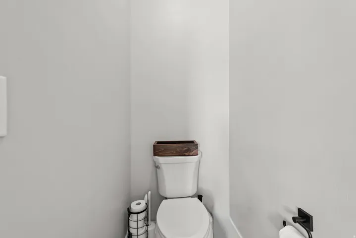 White toilet with a dark wood-finish top accent and matte black fixtures