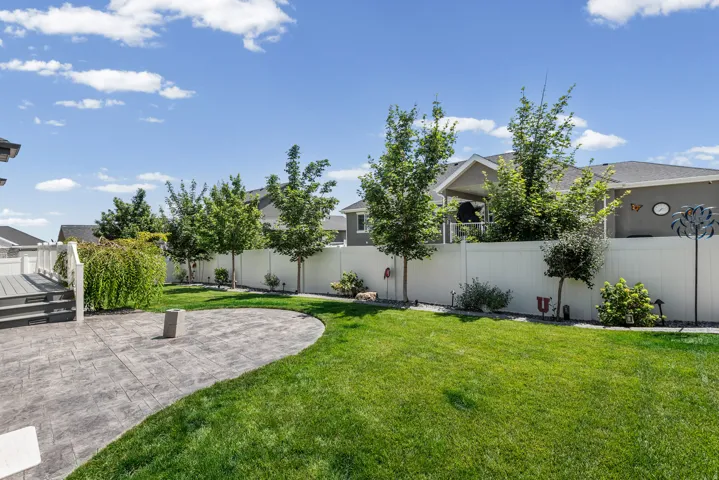Expansive backyard featuring a large stamped concrete patio, a composite deck with white railings, a lush lawn, a privacy fence, and mature landscaping
