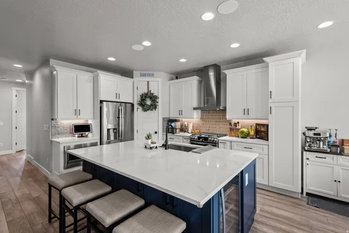 Contemporary kitchen featuring a large central island with a white countertop, white shaker-style cabinetry, stainless steel appliances, a brick-patterned backsplash, and recessed lighting