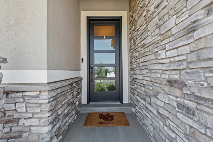 Modern entry door with four lites and dark trim, stone facade, stucco exterior, and concrete porch