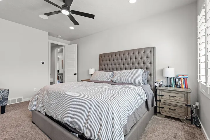 Spacious bedroom featuring plush carpet flooring, a ceiling fan with integrated lighting, recessed lighting, white wall paint, and white plantation shutters