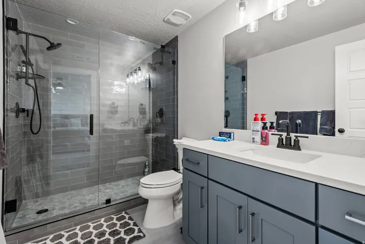 Glass-enclosed shower with subway tile surround, pebble-finish shower pan, and dual shower heads