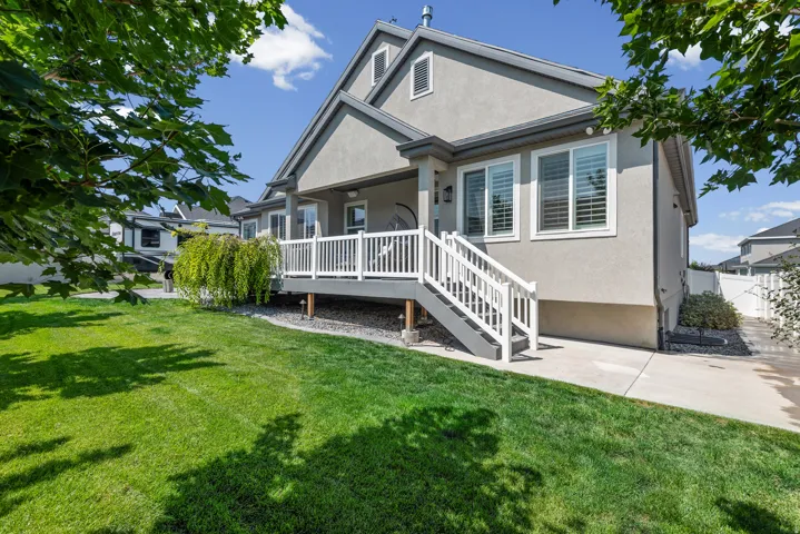 Stucco exterior with a covered patio and white railing, featuring a spacious grass lawn and concrete walkway