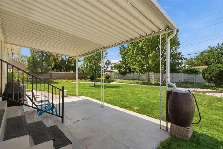 Covered patio with concrete steps, wrought iron railing, and a rain barrel system