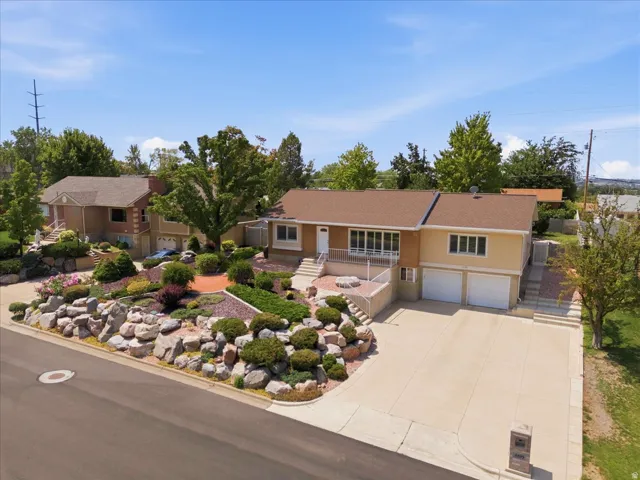 Split-level residence featuring a two-car garage, mature landscaping with stone accents, and a spacious concrete driveway