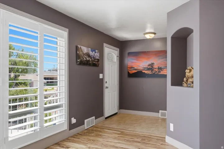 Entryway featuring wood-finish flooring, white plantation shutters, a white paneled door with decorative glass, and a built-in arched wall niche