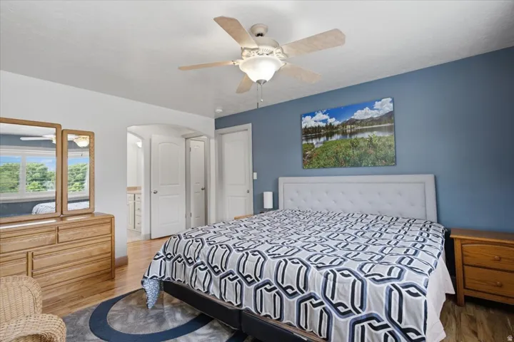 Wood-finish flooring, ceiling fan, arched doorway, and white paneled doors