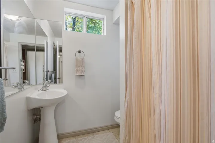 Pedestal sink with chrome faucet, mirrored medicine cabinet, and transom window