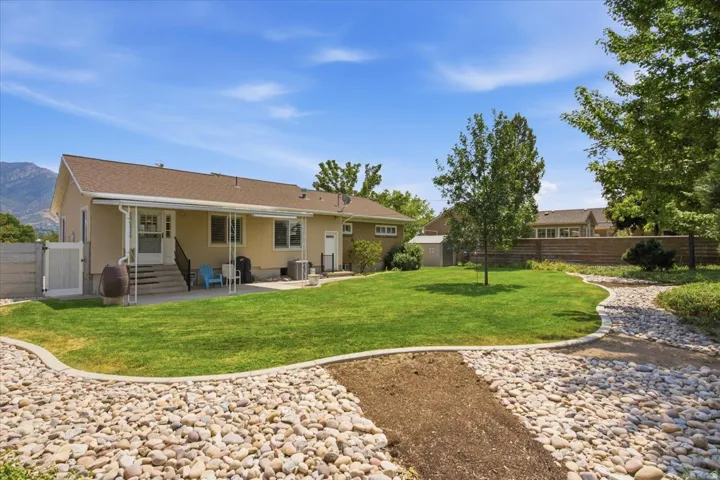 Expansive backyard featuring a manicured lawn, established trees, a paver patio with a covered section, and a decorative pebble pathway