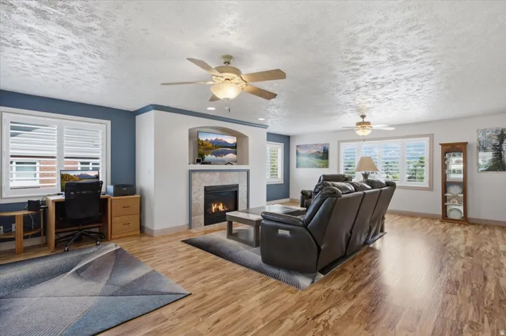 Living area featuring a gas fireplace with a stone surround, built-in media niche, wood-finish flooring, and white plantation shutters