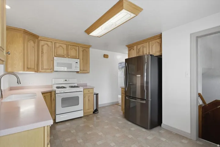 Kitchen featuring wood cabinetry, light countertops, white gas range, and stainless steel refrigerator