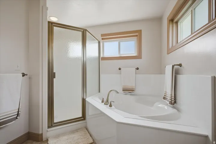 Built-in soaking tub with deck-mounted faucet, framed windows, and a glass-enclosed shower with a bronze frame