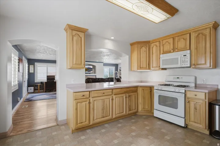 Light wood-finish cabinetry, white built-in microwave, white gas range, and archway entry