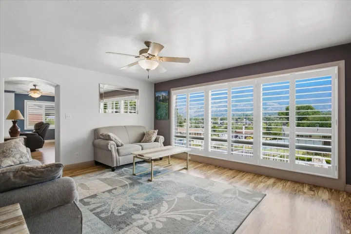 Expansive windows with white plantation shutters, wood-finish flooring, and a ceiling fan with integrated lighting
