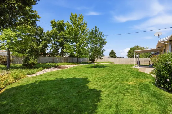 Expansive lawn area with mature trees, a covered patio, and a privacy fence