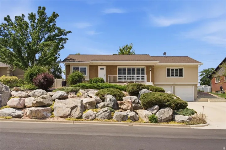 Two-car garage with white doors, light-colored exterior siding, and a prominent rock and shrub landscaping