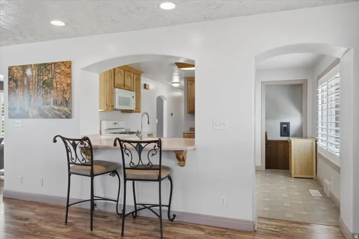 Kitchen bar seating with light-toned countertop, wood-finish flooring, and arched doorways