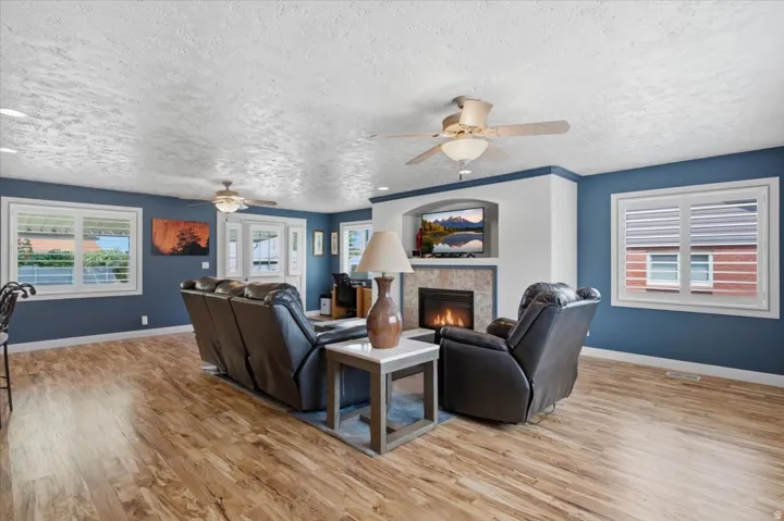 Living area featuring wood-finish flooring, a built-in fireplace with stone surround, and multiple windows with plantation shutters
