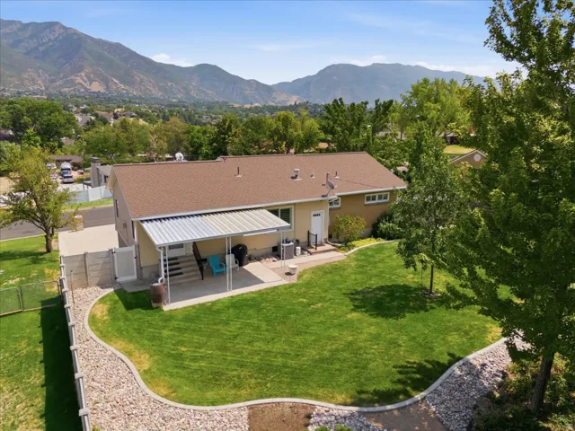 Expansive rear yard featuring a covered patio, paved walkway, and mountain backdrop