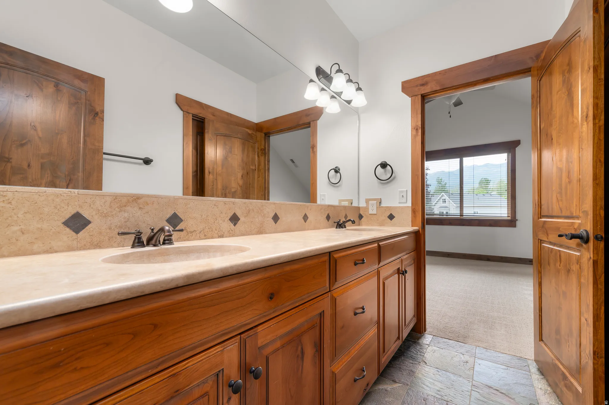 Dual vanity with integrated sinks, stone countertop with decorative tile backsplash, wood-finish cabinetry, and stone tile flooring