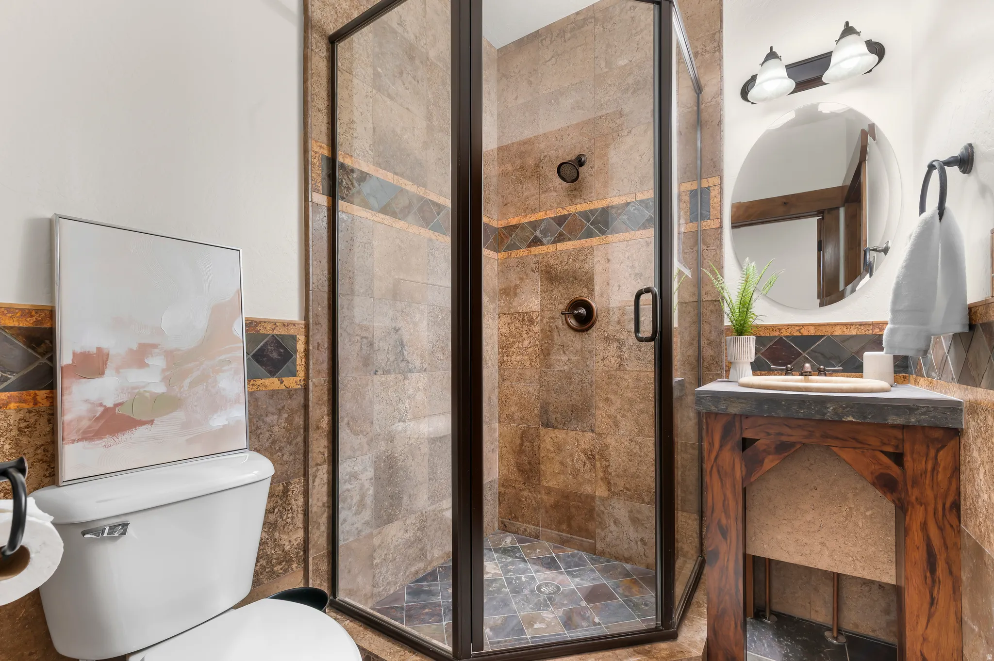Corner shower with bronze-framed glass enclosure, stone-tiled walls, and a mosaic tiled floor