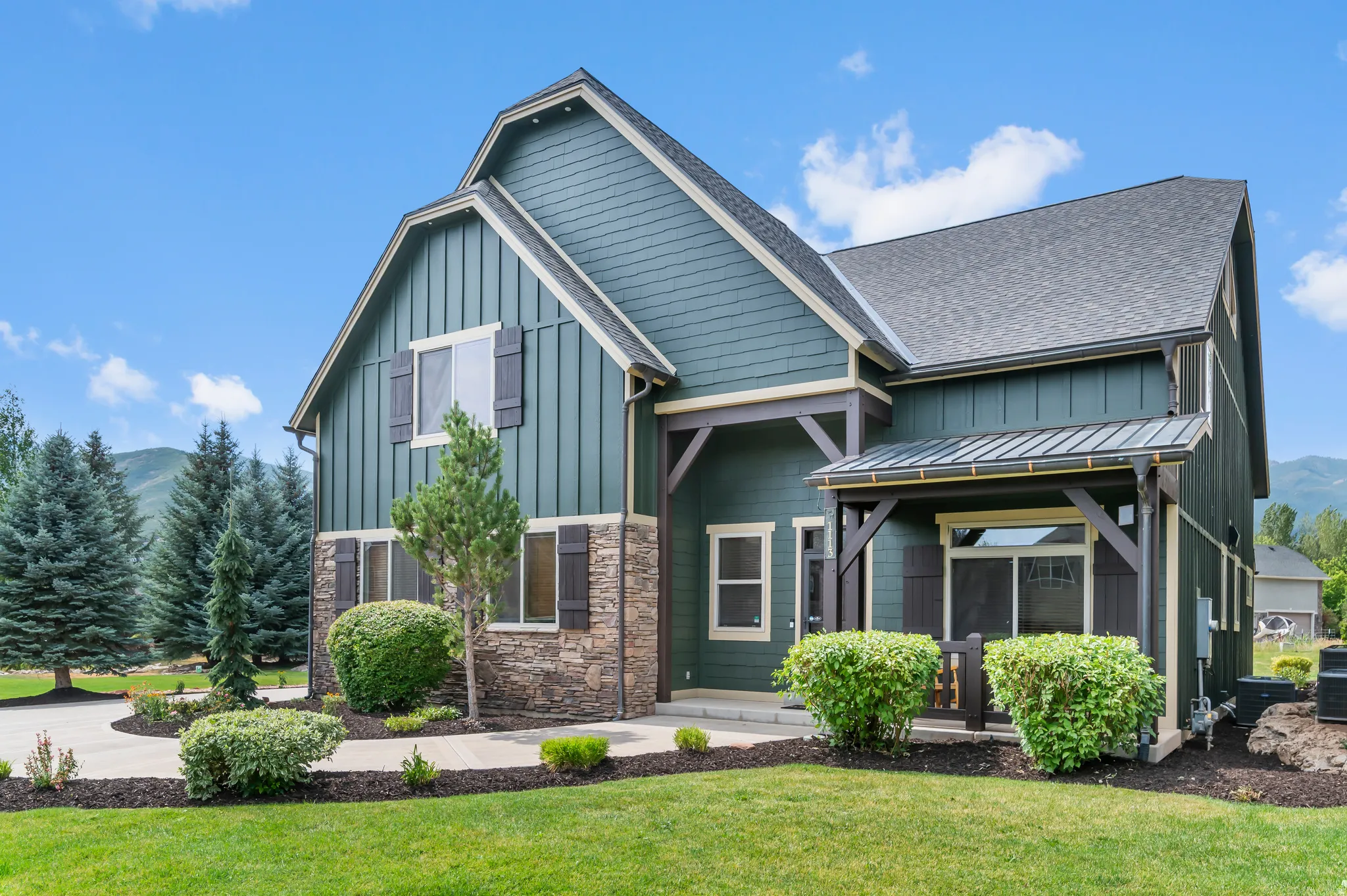 Gable roofline, board and batten siding, stone facade, covered entry, and a paved driveway