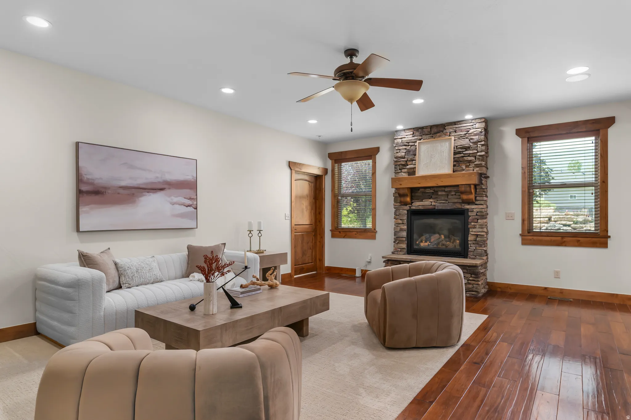 Stone-faced fireplace with a wood mantle, wood-finish flooring, and recessed lighting