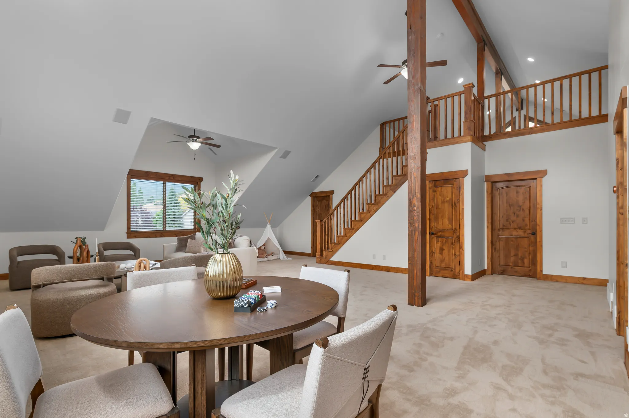Vaulted ceiling with exposed wood beams, wood-trimmed windows, recessed lighting, and a wood staircase with a matching railing