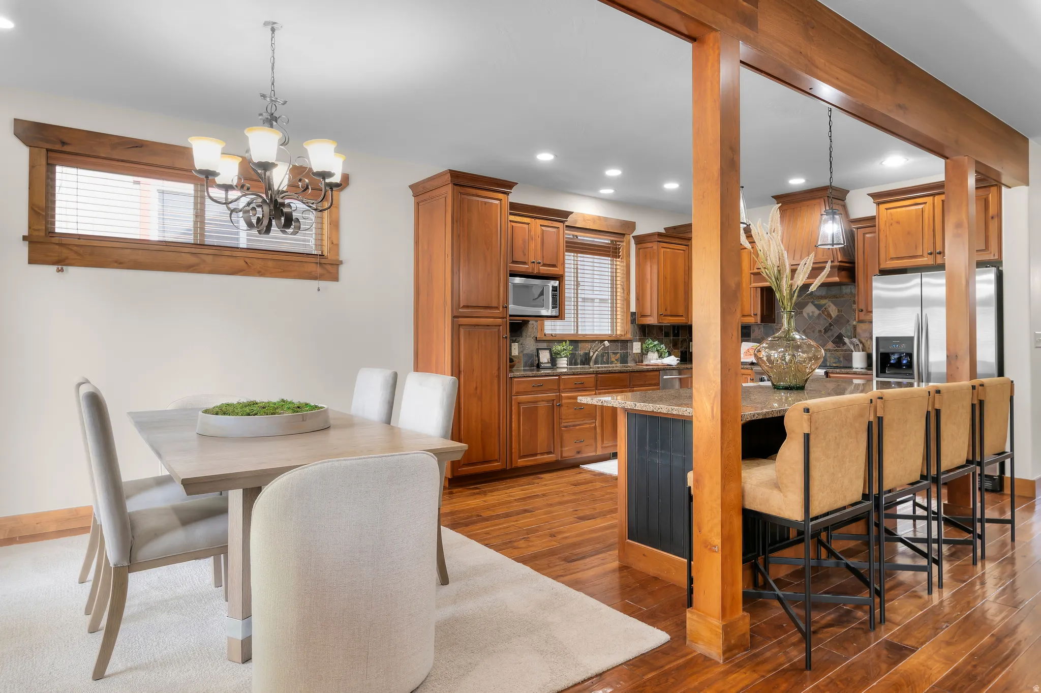 Hardwood flooring, wood-toned cabinetry, stainless steel appliances, kitchen island with seating, and a decorative chandelier
