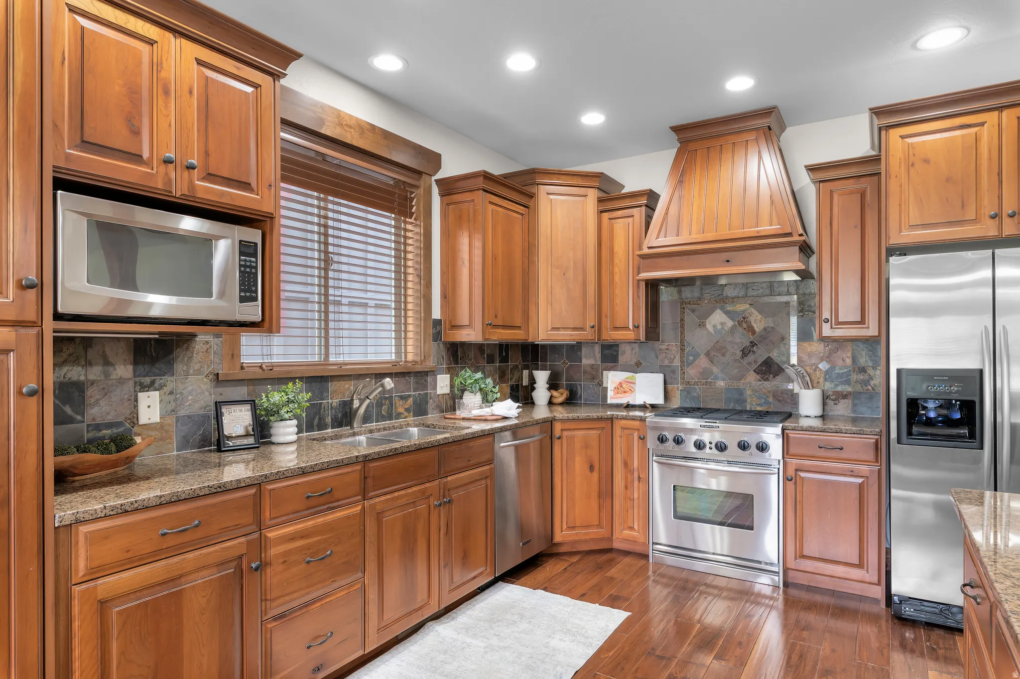 Kitchen featuring wood cabinetry, stainless steel appliances, granite countertops, and wood-finish flooring