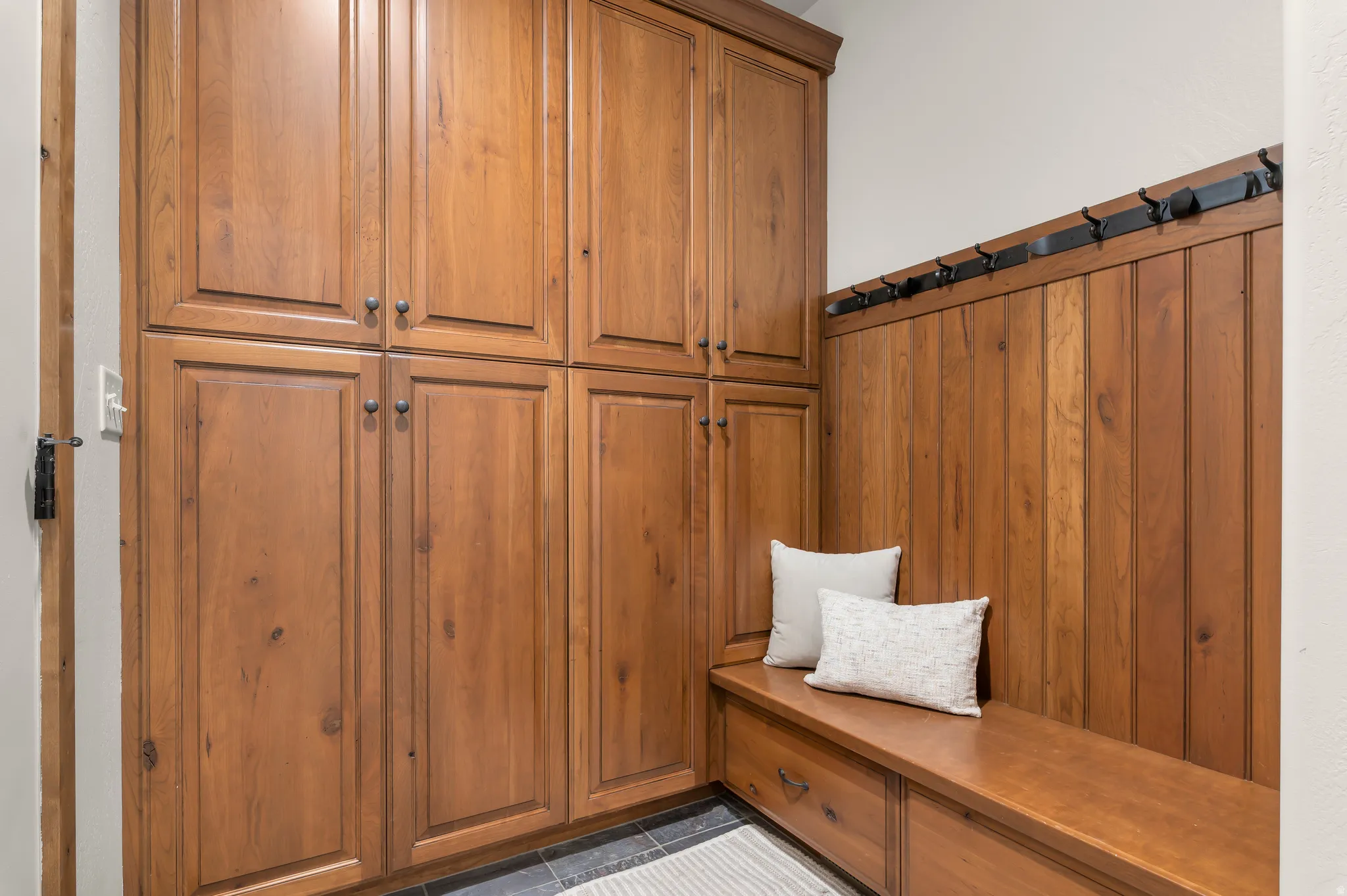 Built-in cabinetry with wood paneling, integrated storage bench, and wall-mounted coat hooks